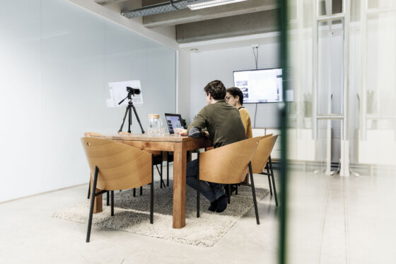 Een man achter een laptop met een vrouw ernaast met een camera op hen gericht